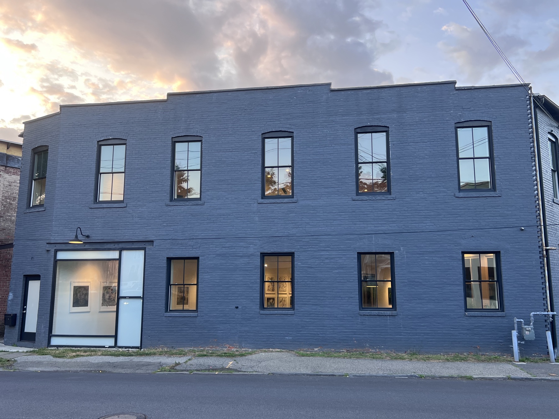 76 Prince Street at last light, windows lit and artwork visible in the storefront gallery