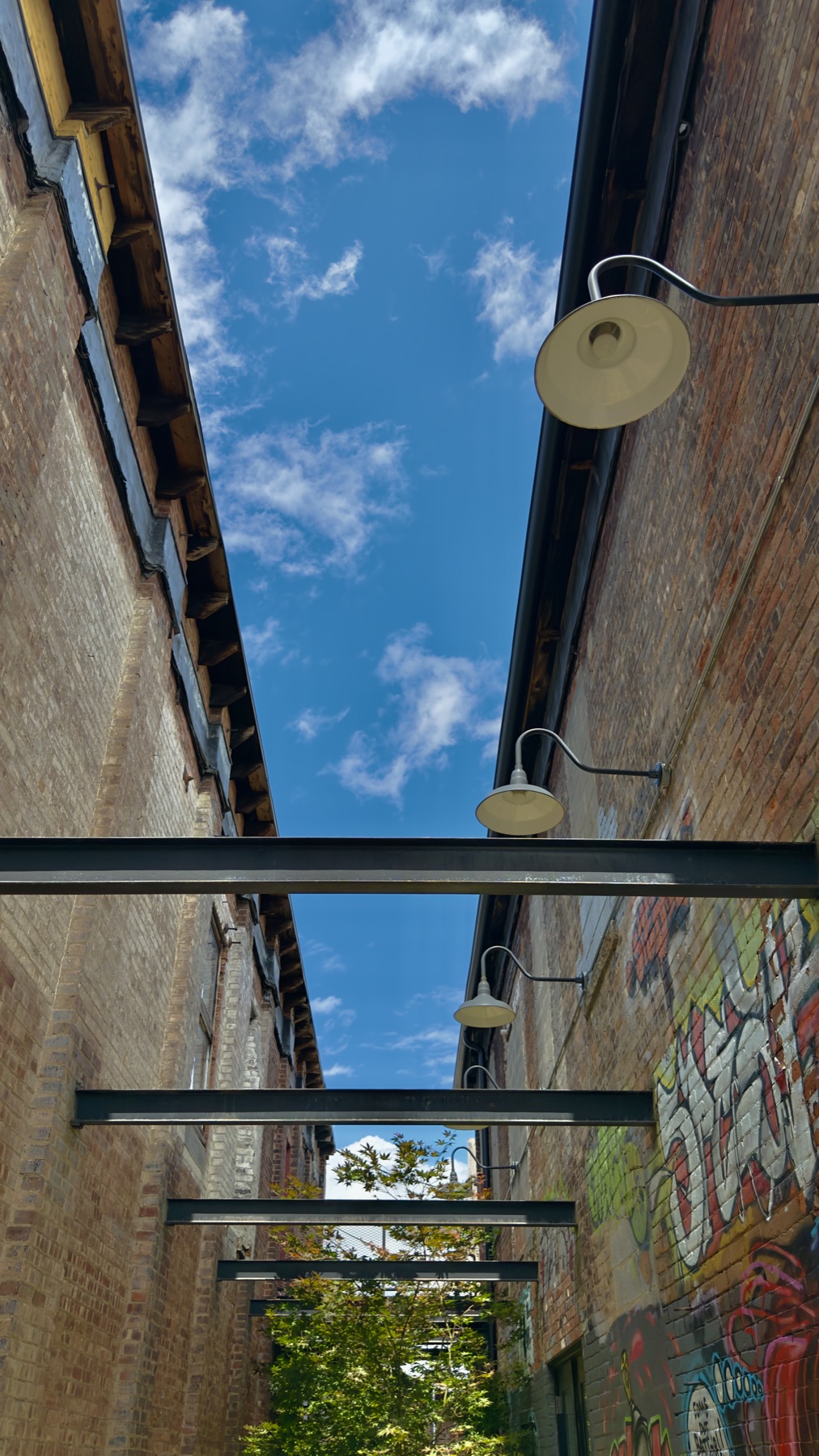 Brick alley with steel beams and gooseneck lamps under a blue sky
