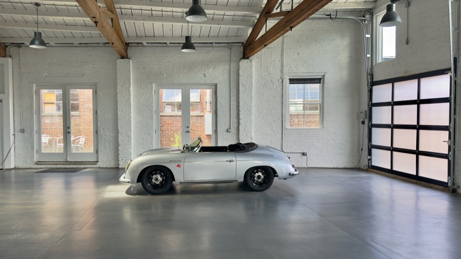Silver Porsche 356 Speedster in profile by the glass drive-in bay